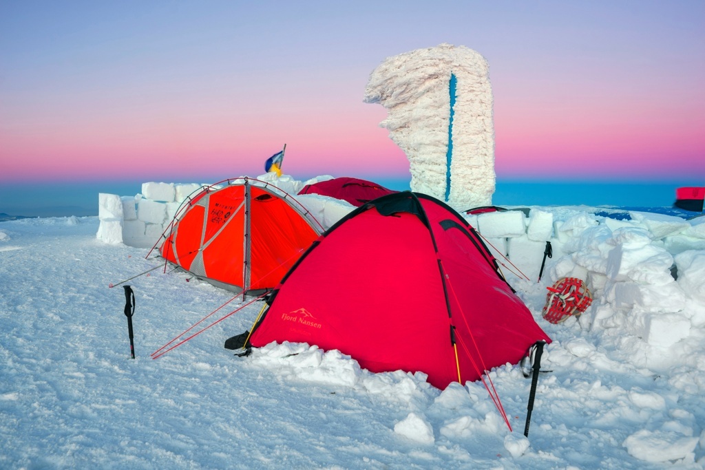 Namioty otoczone ścianami śnieżnymi na zimowym campingu przy zachodzie słońca.