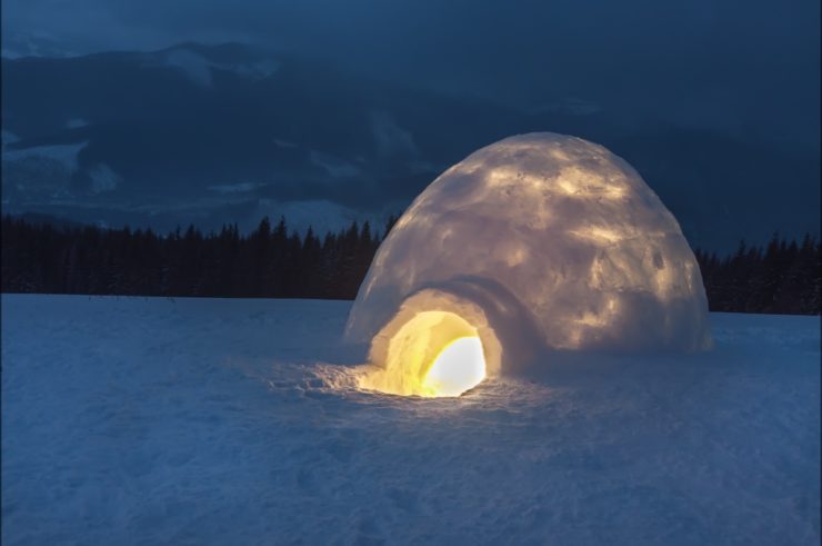 Oświetlone igloo nocą w ośnieżonym krajobrazie górskim.